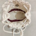 Handmade macrame potli bag in white with drawstring closure styled with casual outfit on wooden table