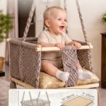 Baby sitting in white macrame baby swing with wooden base and cushion indoors